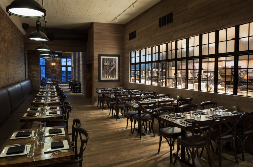 A moody, industrial style dining room lined with windows inside Firewood on Main, one of the best restaurants in Park City, Utah.